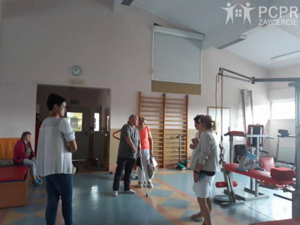 Zdjęcie: Grupa kobiet i mężczyzn na sali gimnastycznej ogląda sprzęt rehabilitacyjny taki jak rowerki, rotory, wyciągi